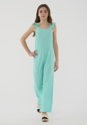 Jumpsuit verde menta con tessuto testurizzato, design a gamba larga e spalline volanti. Abbinato a espadrillas beige con dettagli neri.