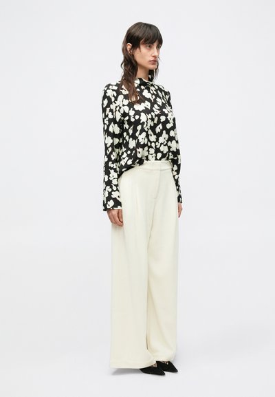 Czarna bluzka z długim rękawem w biały kwiatowy wzór, zestawiona z kremowymi spodniami o szerokich nogawkach i czarnymi, spiczastymi butami. Gładka tkanina, luźny krój.