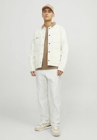 White denim jacket with snap buttons, brown corduroy collar, beige shirt underneath, white pants, and beige sneakers with a black accent.