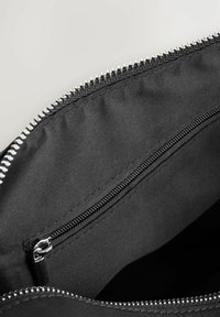 Interior de una bolsa de tela negra con un bolsillo con cremallera. El borde superior cuenta con una cremallera de tono plateado. Textura suave y diseño limpio y sencillo.