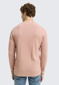 Langarmshirt in lichtroze, textuurstof, ronde hals, effen kleur, gecombineerd met blauwe spijkerbroek; gezien vanaf de achterkant.