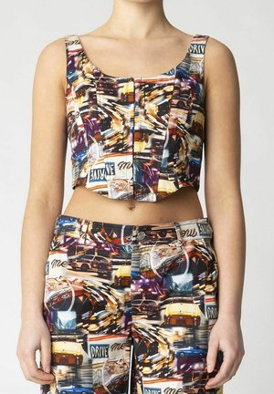 Femme portant un crop top et un pantalon assortis avec un imprimé coloré de voiture vintage et panneau de rue, mains détendues sur les côtés.