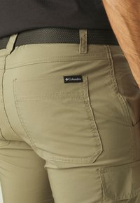 Beige cargo bukser med en glat tekstur og dobbelt lomme bagpå, med et Columbia-logo mærke og et sort vævet bælte.