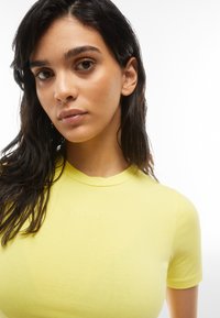 Keltainen lyhythihainen t-paita kevyestä kankaasta, jossa on istuva muotoilu. Siinä on pyöreä pääntie ja hienovarainen "Freddy"-brändäys edessä.