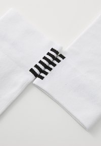 Weiße Sportsocken mit strukturierter Oberfläche, versehen mit schwarzen Streifenakzenten an den Bündchen. Sauberes, minimalistisches Design, geeignet für den Sport.