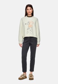 Pulli in hellcreme mit einer Cartoon-Hund-Illustration in Orange und schwarzem Umriss. Kombiniert mit dunkelgrauen, schmal geschnittenen Jeans und braunen Slip-Ons.