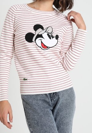 Chemise à manches longues rayée blanche et rouge avec un grand dessin de souris cartoon souriante portant une casquette sur la poitrine, associée à un jean bleu délavé.