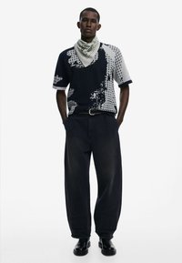 T-shirt med kort ærme i sort og grå med abstrakte mønstre, parret med løse, mørke denimbukser. Accessoriseret med et lyst bandana.
