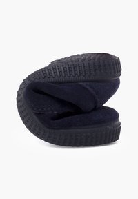 Zapatilla de color azul marino con parte superior de tela suave, suela de goma y fondo texturizado. La zapatilla está doblada para mostrar su diseño y material.