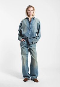 Jeansoutfit med en löst sittande, ljusblå skjorta med knappar och matchande vida jeans. Texturerat tyg med blekta detaljer och en avslappnad design.