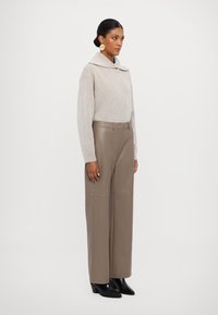 Lys beige, ribbestrikket genser med høy krage, kombinert med vide taupe-bukser. Modellen har på seg svarte spisse ankelstøvler og store sirkulære øreringer.