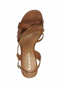 Sandale en simili cuir marron avec des sangles entrecroisées, une fermeture à boucle et une finition semi-brillante. Semelle plate avec le nom de la marque embossé à l'intérieur.