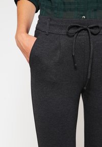 Szare spodnie dresowe z regulowanym sznurkiem w pasie, bocznymi kieszeniami i teksturowanym materiałem. Krój luźny, odpowiedni do noszenia na co dzień.