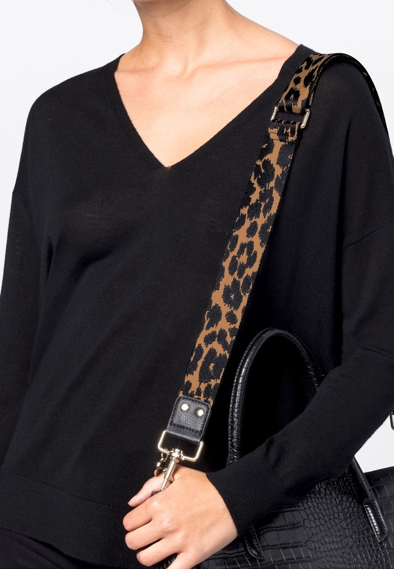 Femme portant un pull col V noir avec un sac à main noir texturé doté d'une bandoulière imprimé léopard marron et noire.