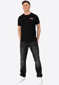 Must mustaga mustre ja punase ja valge äärepitsiga, rinnal logo, koos tumedate teksade ja valgete tenistega.