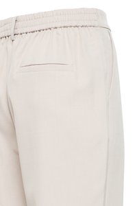 Pantalon beige avec taille élastique, passants de ceinture et une seule poche passepoilée au dos côté droit.