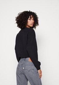 Felpa nera corta con maniche lunghe, scollatura rotonda e trama morbida. Abbinata a jeans grigi a vita alta con un patch in pelle.
