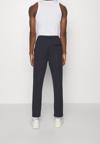 Czarne zwężane dresy z elastycznym paskiem, z tylną kieszenią i miękkiego materiału. Noszone z białym topem na ramiączkach i trampkami.