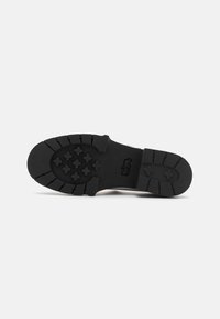 Semelle de chaussure en caoutchouc noir avec une surface texturée, présentant un motif en zigzag et des crampons en forme d'étoile pour une meilleure traction. Le design est fonctionnel et durable.