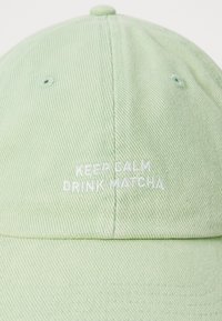 Svetlo zelena baseball kapa z belo vezenim napisom "OHRANI MIR, PIJ MATCHO" na sredini sprednje plošče.