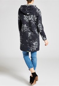 Navy dlouhý kabát s květinovým potiskem a kapucí, s vypasovaným pasem a dvěma bočními kapsami, doplněný o potrhané modré džíny a černé kotníkové boty.