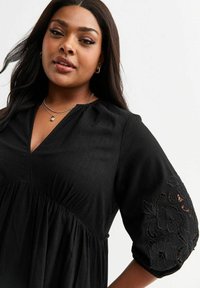 Black, knee-length dress with short, puffed sleeves. Features embroidered floral patterns on sleeves and a V-neck design. Soft texture.