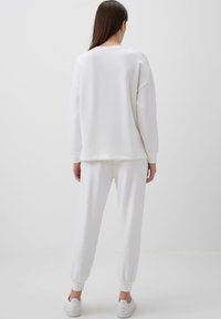 Completo in felpa bianca composto da felpa e pantaloni jogger realizzato in tessuto morbido. Vestibilità comoda con polsini e caviglie a costine, caratterizzato da un design minimalista e senza motivi.