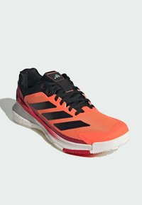 Atletické boty s růžovo-oranžovým síťovým svrškem, černými akcenty a třemi černými pruhy. Obsahují polstrovanou bílou podrážku a texturovanou gumovou podrážku.