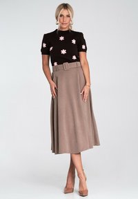 Czarny dzianinowy top z różowym haftem kwiatowym, zestawiony z brązową spódnicą o wysokim stanie z plisami, która posiada pasek z klamrą. Beżowe obcasy dopełniają stylizację.