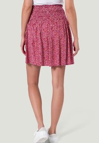 Falda corta de algodón con cintura fruncida, que presenta un patrón de hojas rojas y rosas. El diseño recortado y la tela fruncida añaden textura.