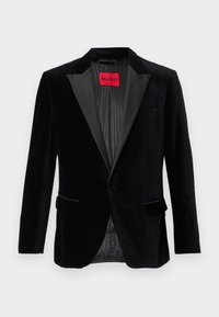 Črn žametni blazer z satenskim ovratnikom, zapiranje na en gumb, dvema sprednjima žepoma in podloženo notranjostjo, ki vsebuje rdečo oznako blagovne znamke.