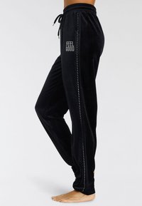 Schwarze Samtjogginghosen mit einem Kordelzugbund, seitlich verziert mit kleinen Nieten und dem Text "FEEL GOOD" in Diamanten.