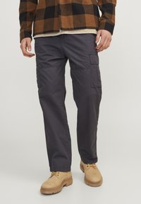 Cargo bukser i mørkegrå stof, med flere sidelommer, en afslappet pasform og lige ben-design. Båret med brune snørebunds støvler.