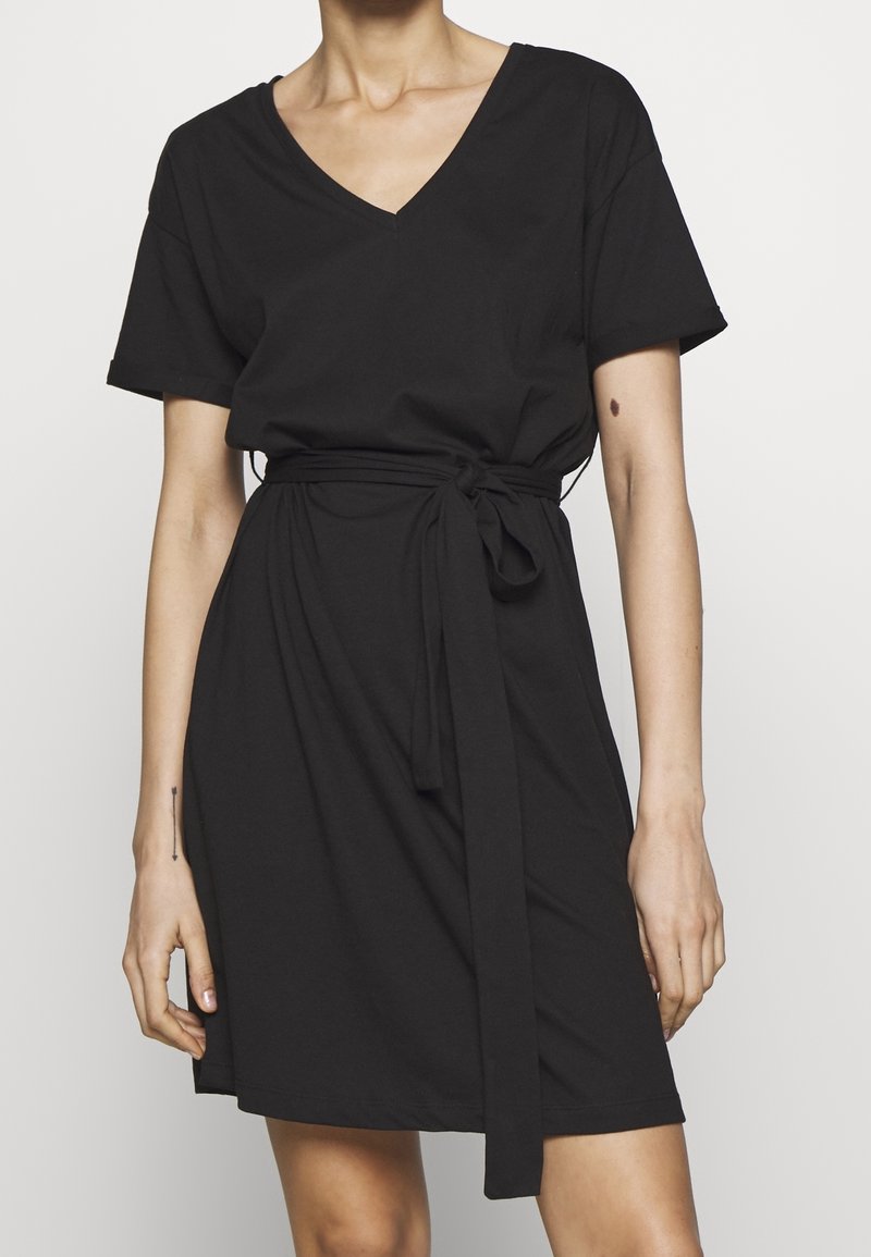 Czarna sukienka krótki rękaw z miękkiego materiału, z dekoltem w kształcie litery V i paskiem w talii, charakteryzująca się luźnym krojem i prostym dołem.