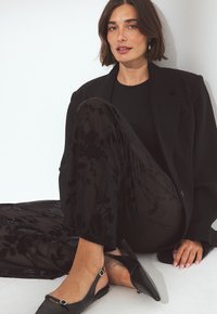 Črn blazer preko prilagojenega črnega topa, v kombinaciji s prosojnimi črnimi hlačami z cvetličnimi vzorci. Črne slingback čevlje z dodatki.