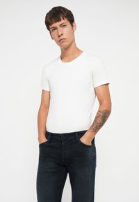 Camiseta blanca de manga corta combinada con jeans azul oscuro. La camiseta tiene un escote redondo y los jeans presentan un ajuste clásico con bolsillos.