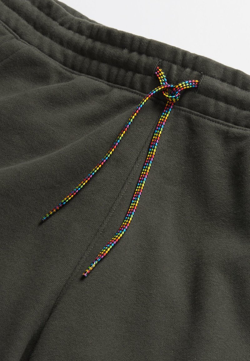 Pantaloni con vita elastica grigio scuro e coulisse intrecciata colorata annodata a fiocco, che mostrano la trama del tessuto e i dettagli delle cuciture.
