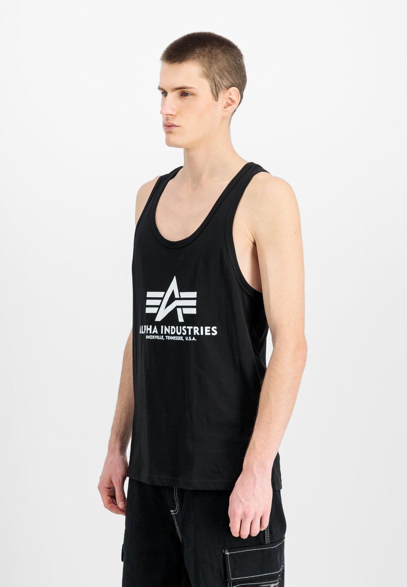 Black tank top made of cotton, featuring a prominent white logo and text "ALPHA INDUSTRIES." Design includes wide straps and a relaxed fit.