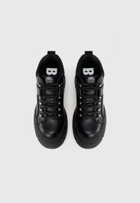 Melnas kedas ar gludu ādas augšdaļu, apaļu purngalu, biezu gumijas zoli, metāliskiem acīm un logotipu uz mēles.