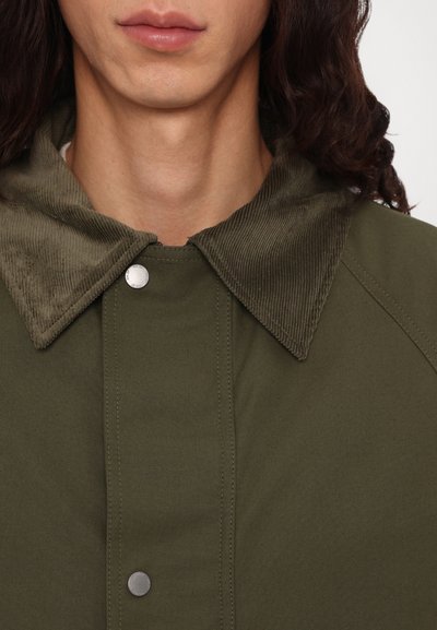Veste vert olive avec un col en velours côtelé, fermeture à boutons-pression et texture lisse. Présente un design de col contrastant et des coutures d'épaule.