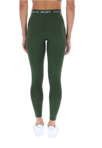Tmavozelené legíny s širokým pásom, na ktorom je nápis "TED BAKER SPORT". Materiál je hladký a strih je priliehavý. Biele tenisky dotvárajú vzhľad.