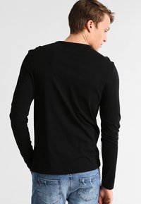 Camisa negra de manga larga con cuello redondo. Textura suave y diseño ajustado, combinada con jeans de mezclilla azul claro.