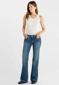 Un débardeur blanc et un jean évasé bleu portés par un mannequin. Le jean présente un design classique à cinq poches et un délavage usé ; texture en denim lisse.