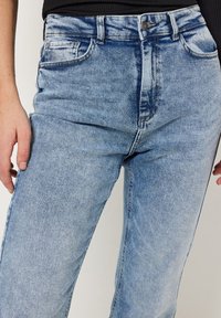 Lichtblauwe denim high-waisted jeans met een vervaagde afwerking. Heeft voorzakken en een rits met knoopsluiting. Klassieke rechte pijpen.
