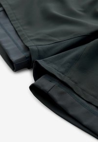 Sportsshort i mørkegrå stof med et tekstureret design, elastisk talje og syede kanter. Nærbillede, der fremhæver lag.
