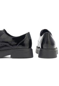 Pantofi din piele neagră cu un finit lucios, vârf rotund �și talpă joasă din cauciuc negru. Prezintă o textură lustruită și accente de cusătură subtile.