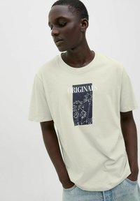 Lichtgroene katoenen t-shirt met een zwart grafisch ontwerp van palm bomen en de tekst "ORIGINALS" in het wit. Korte mouwen, ronde hals ontwerp.