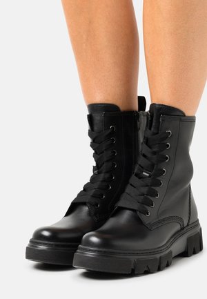 Sorte læder ankelstøvler med tykke gummisåler, snørebånd foran og en sideskade. Har rund tå og polstret krave.