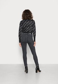 Suéter negro con logo blanco repetido, jeans gris de talle alto con franjas laterales y botines negros con tacón cuadrado.
