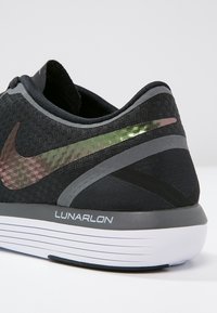 Black athletic shoe featuring a textured fabric upper, metallic accents, grey side stripes, and a cushioned Lunarlon sole.
